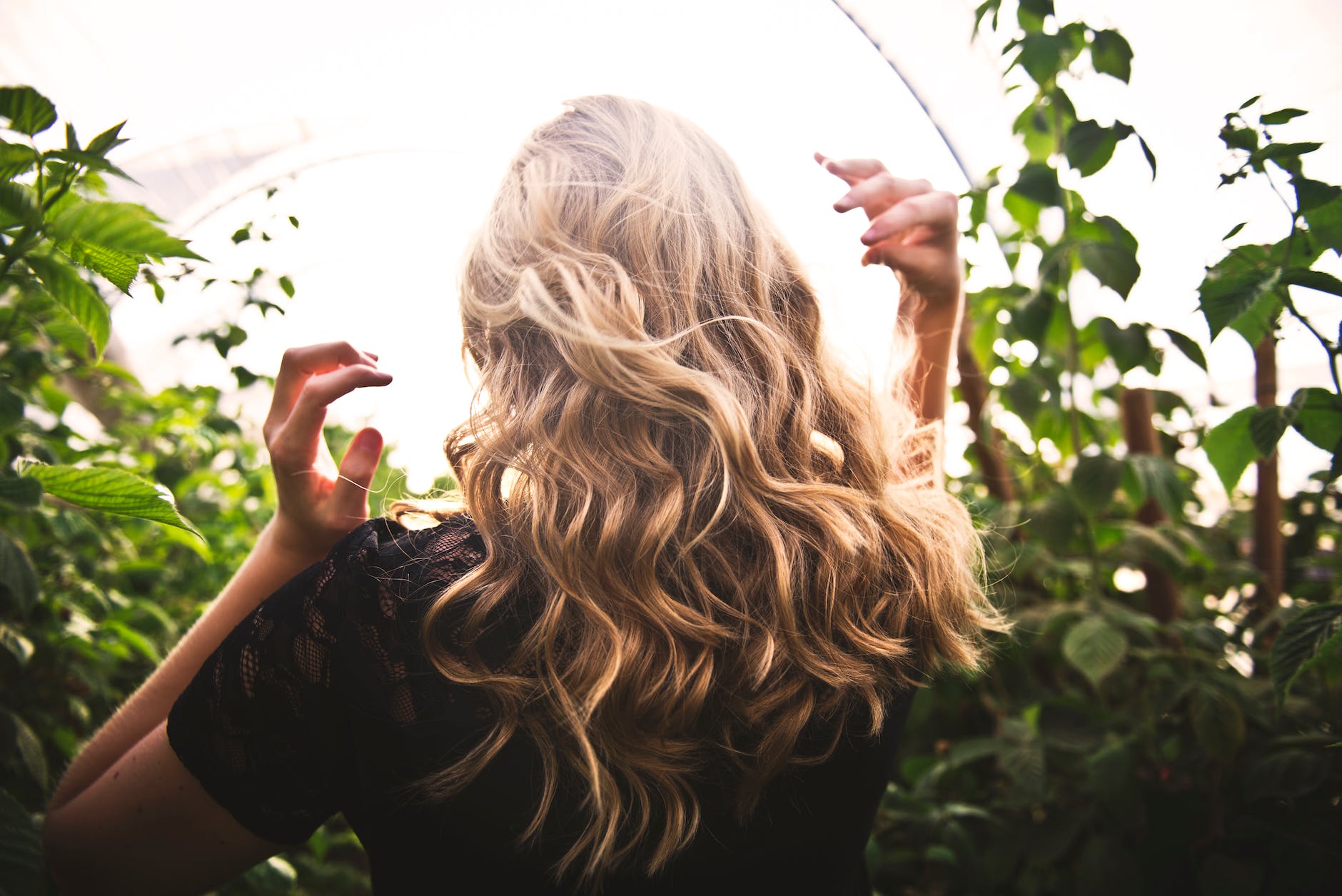 blonde curly wavy haired woman standing between green plants